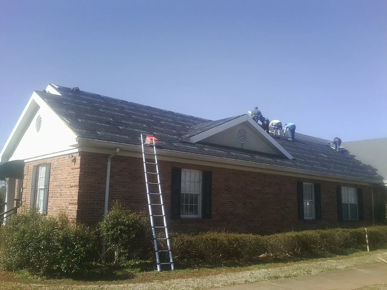 Crew tearing shingles off a brick ranch roof with a ladder set — Emergency Roof Repair work by our crew in Union
